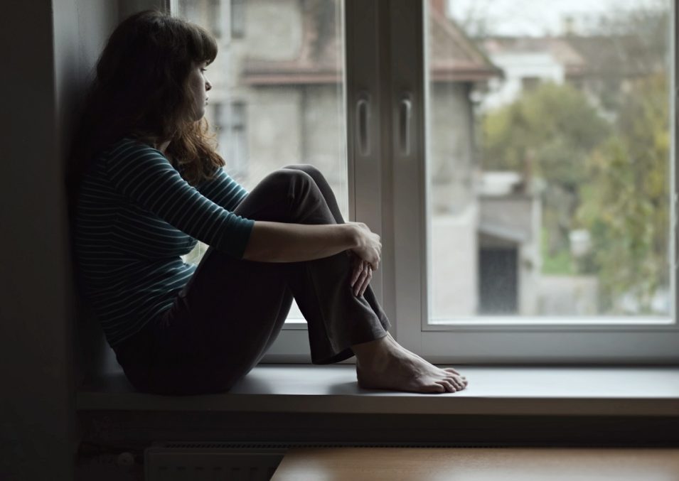 Sad young woman sitting on the window